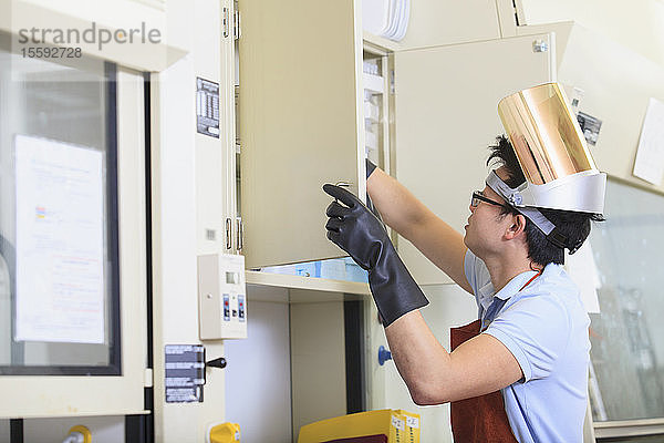 Ingenieurstudent mit Schutzausrüstung auf der Suche nach Material in einem Chemielabor