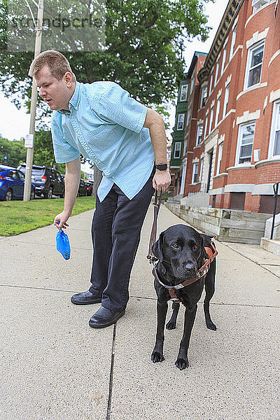 Mann mit Sehbehinderung steht mit seinem Diensthund