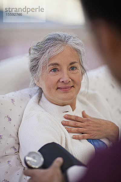 Hoffnungsvolle ältere Frau schaut einen Pfleger an  während ihr Blutdruck gemessen wird