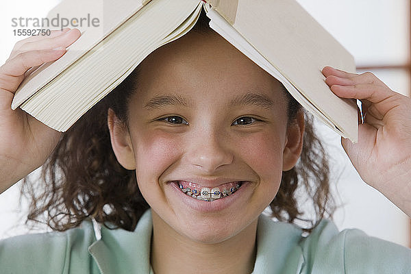Porträt eines hispanischen Mädchens  das sich ein Buch auf den Kopf legt und lächelt