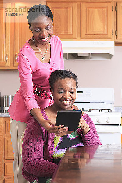 Zwei Schwestern schauen in der Küche auf ein digitales Tablet  eine davon mit einer Lernbehinderung