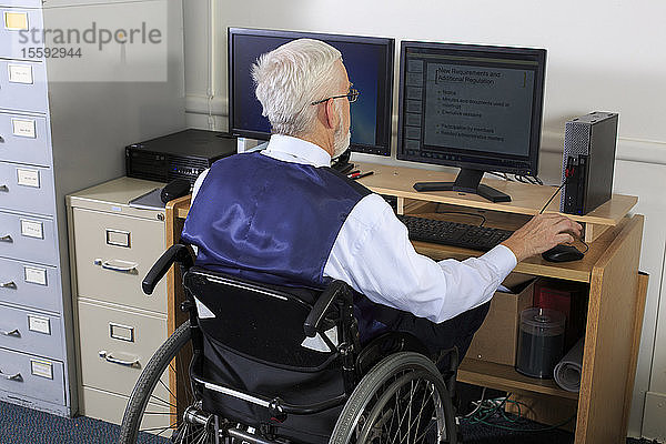 Mann mit Muskeldystrophie im Rollstuhl bei der Arbeit in einem Büro