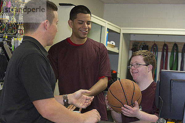 Junger Mann mit Down-Syndrom verteilt Basketball an seine Freunde in der Ausgabestelle für Sportgeräte am College