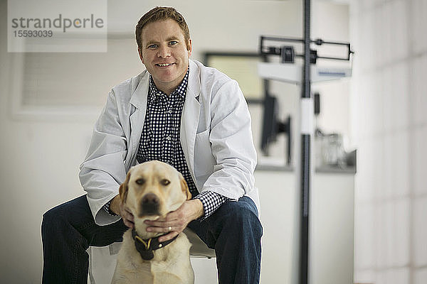 Porträt eines lächelnden Arztes  der einen Hund in einem Untersuchungsraum streichelt