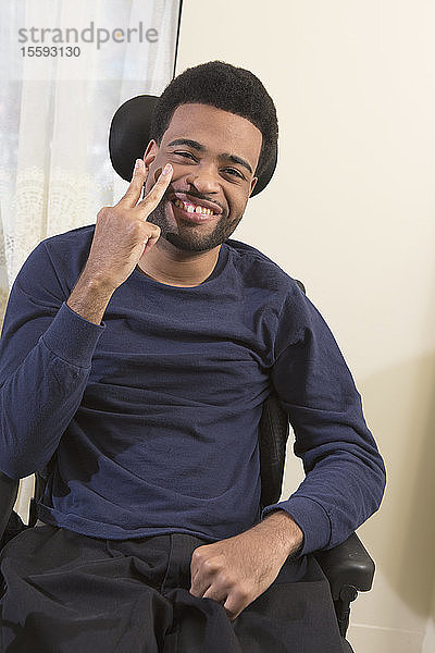 Porträt eines glücklichen afroamerikanischen Mannes mit zerebraler Lähmung  der zu Hause im Rollstuhl gestikuliert