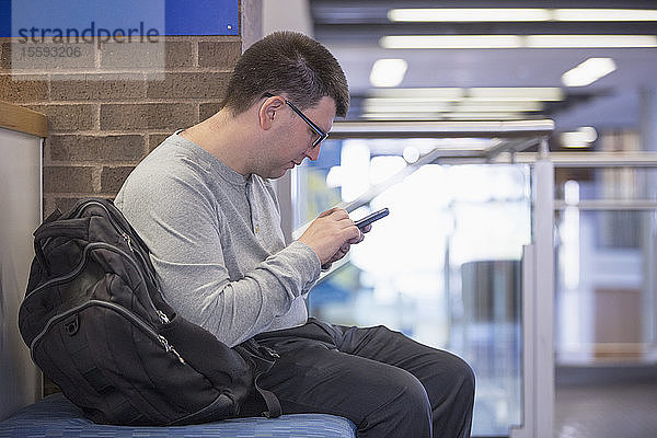 Mann mit Sehbehinderung sitzt in der Schule und benutzt sein Handy