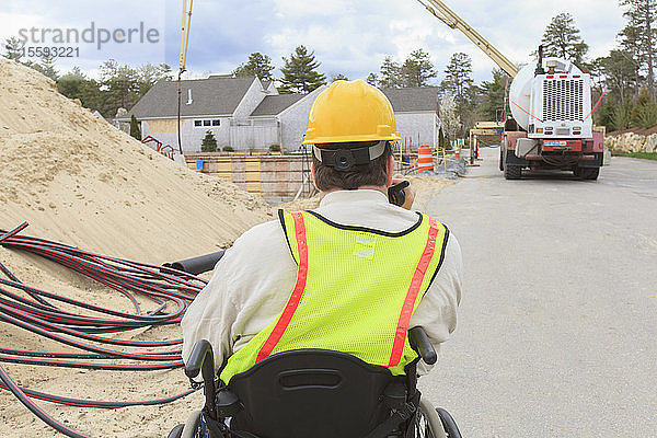 Bauleiter mit Querschnittslähmung am Walkie-Talkie zur Betonpumpe beim Gießen des Fundaments