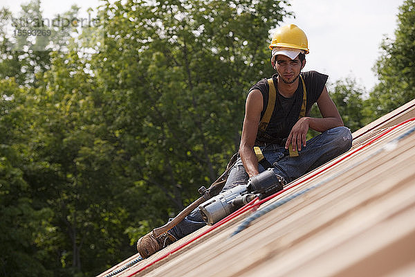 Spanischer Zimmermann  der sich mit einer Nagelpistole auf der Dachkonstruktion eines Hauses ausruht