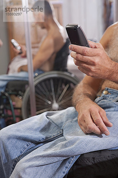 Mann mit Rückenmarksverletzung im Rollstuhl  der ein Mobiltelefon benutzt
