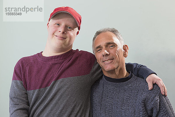 Porträt eines glücklichen jungen Mannes mit Down-Syndrom und seines Vaters mit Rückenmarksverletzung zu Hause