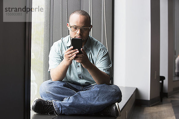 Afroamerikanischer Mann mit Down-Syndrom schaut auf sein Handy