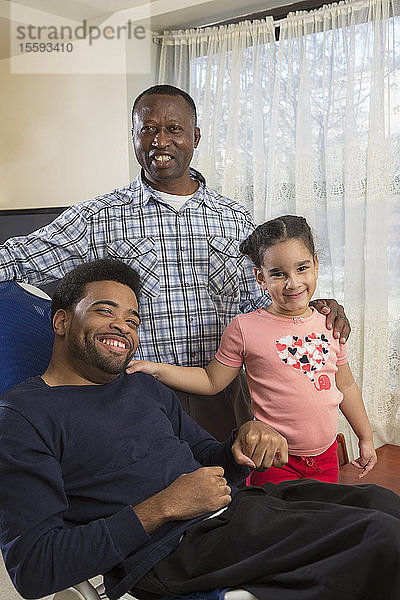 Afroamerikanischer Mann mit zerebraler Lähmung mit seiner Tochter und seinem persönlichen Pflegeassistenten zu Hause