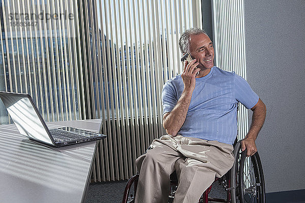 Mann mit Querschnittslähmung im Rollstuhl telefoniert in einem Büro