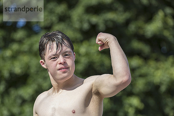 Porträt eines jungen Mannes mit Down-Syndrom  der seinen Bizeps auf einem Steg zeigt