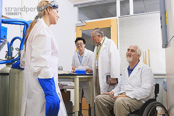 Professor mit Muskeldystrophie bespricht mit einem Ingenieurstudenten und einem Professor das Logbuch für ein Wasserdestillationssystem in einem Labor