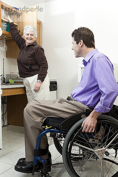 Haushaltshilfe holt ein Glas für einen Mann im Rollstuhl mit Rückenmarksverletzung