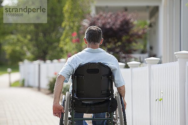 Mann mit Querschnittslähmung im Rollstuhl auf einem Vorstadtspaziergang mit Häusern