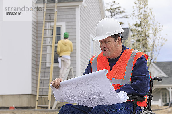 Bauingenieur mit Rückenmarksverletzung mit Hausplänen auf der Baustelle