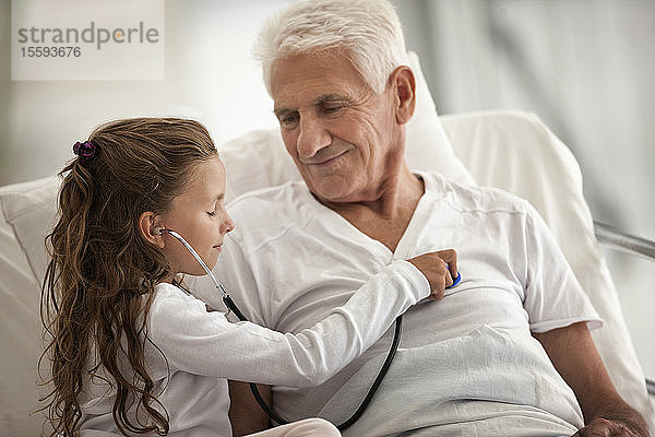 Älterer Mann erhält im Krankenhaus Besuch von seiner Enkelin  die mit einem Stethoskop spielt