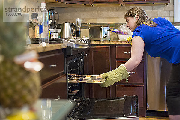 Junge Frau mit Zerebralparese schiebt ein Blech mit Keksen in den Ofen