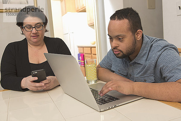 Afroamerikanischer Mann mit Down-Syndrom benutzt mit seiner Mutter zu Hause einen Laptop