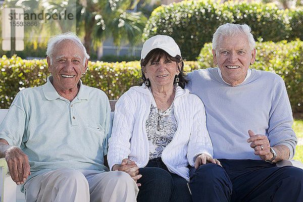 Drei ältere Freunde sitzen auf einer Parkbank und lächeln
