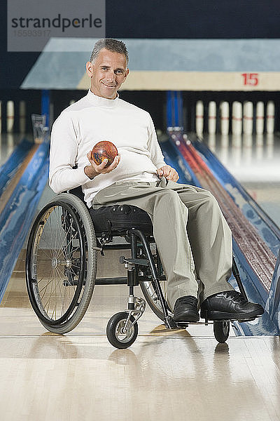 Porträt eines reifen Mannes mit einer Wirbelsäulenverletzung  der eine Bowlingkugel hält und lächelt