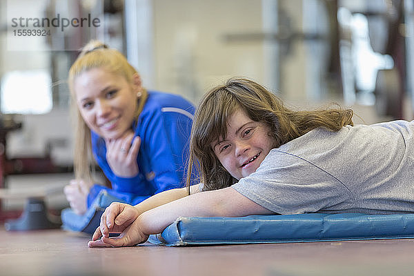 Junge Frau mit Down-Syndrom trainiert mit ihrem Trainer auf einer Übungsmatte im Fitnessstudio