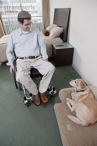 Mann im Rollstuhl mit Rückenmarksverletzung und Diensthund in einem Schlafzimmer