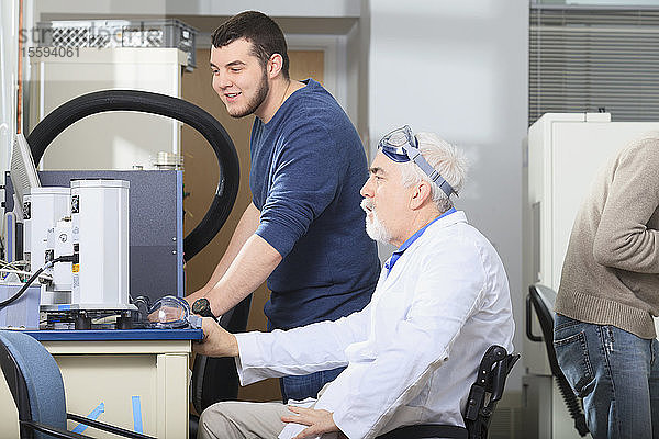 Professor mit Muskeldystrophie bei der Arbeit an einem Wärmegradientenanalysator mit einem Ingenieurstudenten in einem Labor