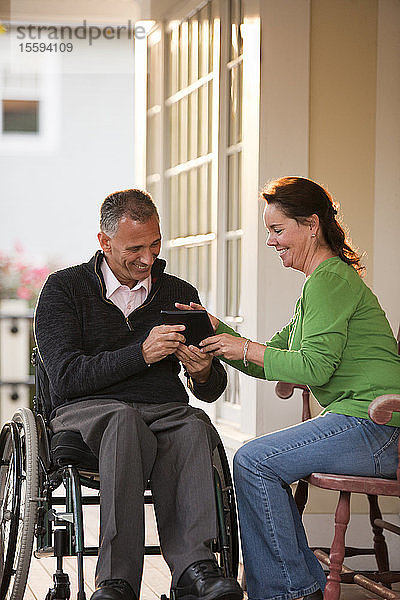 Frau und ihr Mann im Rollstuhl vor ihrem Haus mit einem digitalen Tablet