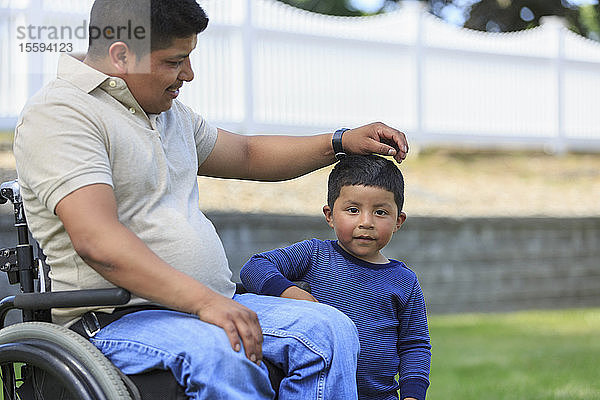 Hispanischer Mann mit Rückenmarksverletzung im Rollstuhl mit seinem Sohn auf dem Rasen