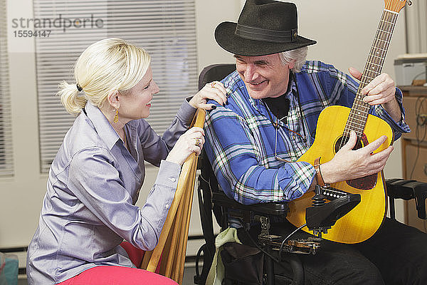 Musiker mit Multipler Sklerose in einem motorisierten Rollstuhl mit seiner Gitarre  der für einen Freund spielt
