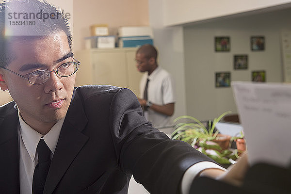 Asiatischer Mann mit Autismus  der in einem Büro arbeitet und nach einer Zeitung greift