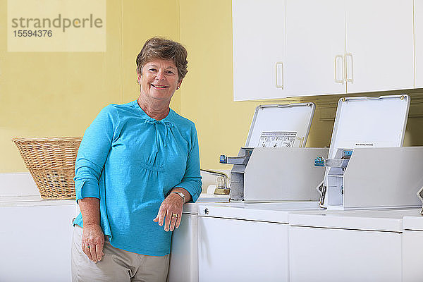 Ältere Frau steht in einer Waschküche vor einer gewerblichen Waschmaschine