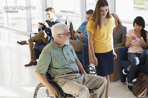 Mann mit Muskeldystrophie im Rollstuhl geht mit einem anderen Passagier in einem Flughafenkorridor spazieren