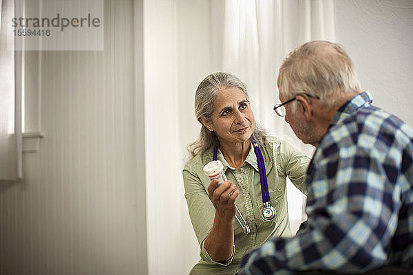Eine Ärztin hört einem älteren männlichen Patienten zu  während sie eine Flasche mit Medikamenten hält