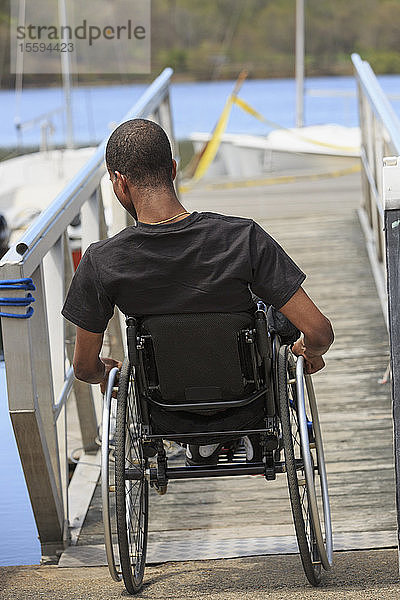 Mann im Rollstuhl  der an Spinaler Meningitis erkrankt war  fährt eine Rampe hinunter zu einem Dock