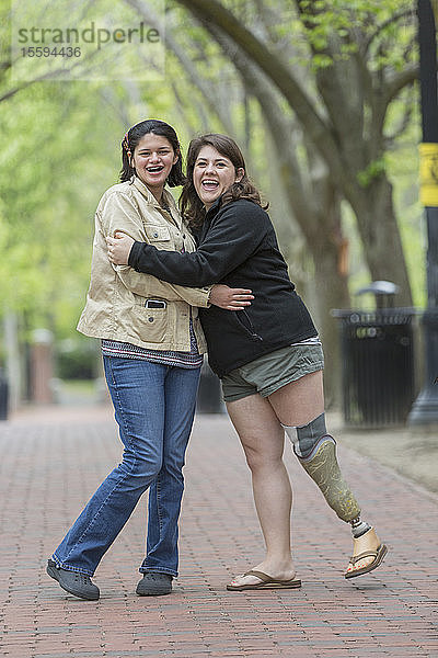 Zwei glückliche junge Freundinnen  die sich umarmen  eine mit einer Beinprothese