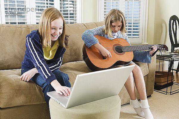 Blick auf zwei Schwestern  die mit einem Laptop und einer Gitarre auf einem Sofa sitzen.