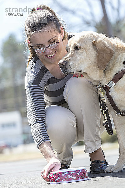 Junge Frau mit einer Sehbehinderung füttert ihren Diensthund