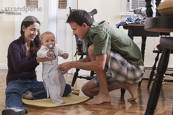 Eltern  die gemeinsam die Kleidung ihres Sohnes wechseln  während sie auf dem Boden sitzen