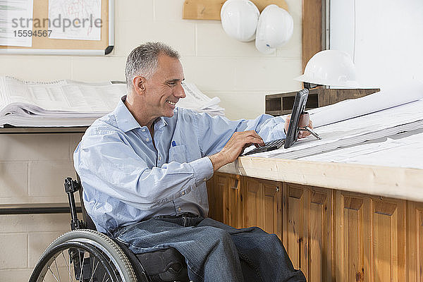 Projektingenieur  der im Rollstuhl sitzend mit einer Rückenmarksverletzung ein Tablet benutzt  um Pläne für die Baustelle zu prüfen