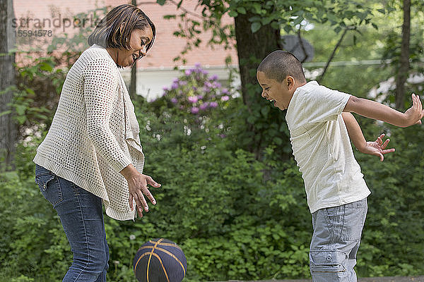 Hispanischer Junge mit Autismus spielt mit seiner Mutter im Park mit einem Ball