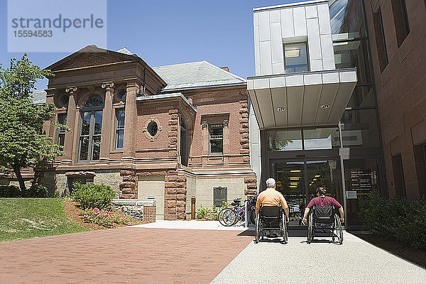 Rückansicht von zwei Menschen mit Muskeldystrophie vor einem Bibliotheksgebäude