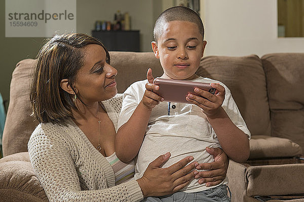 Hispanischer Junge mit Autismus spielt mit seiner Mutter zu Hause ein elektronisches Spiel