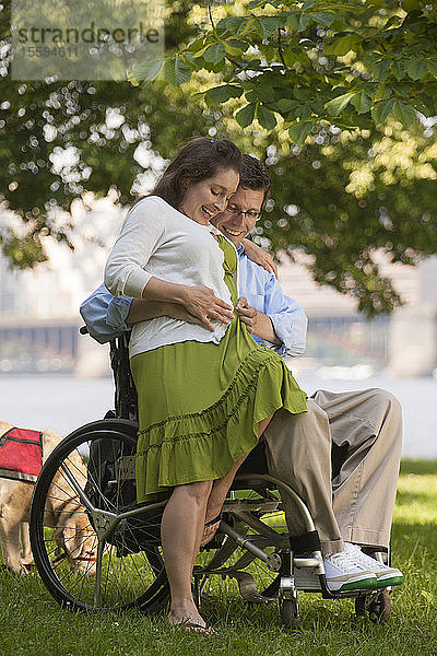 Mann mit einer Rückenmarksverletzung im Rollstuhl fühlt den Babybauch seiner Frau