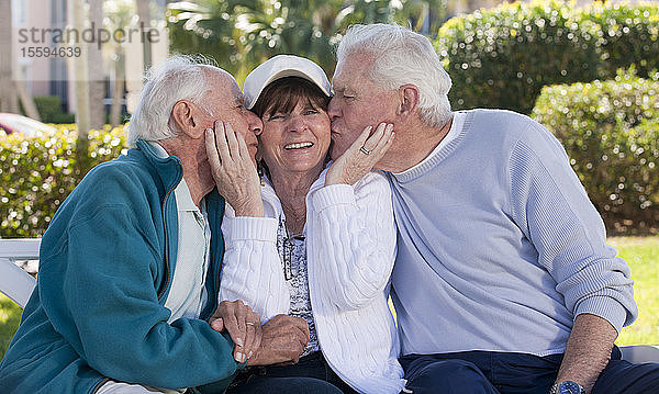 Zwei ältere Männer  die ihre Freundin in einem Park küssen