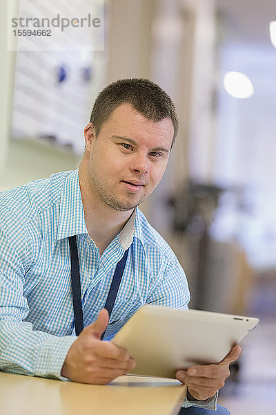 Junger Mann mit Down-Syndrom arbeitet als Krankenhaushelfer mit seinem Tablet