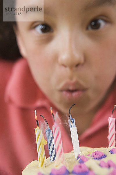 Hispanisches Mädchen bläst Kerzen auf einer Geburtstagstorte aus